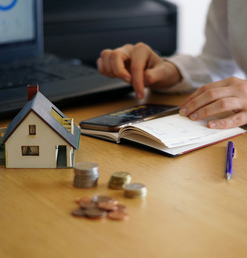 Model house and coins on a desk while a homeowner reviews expenses