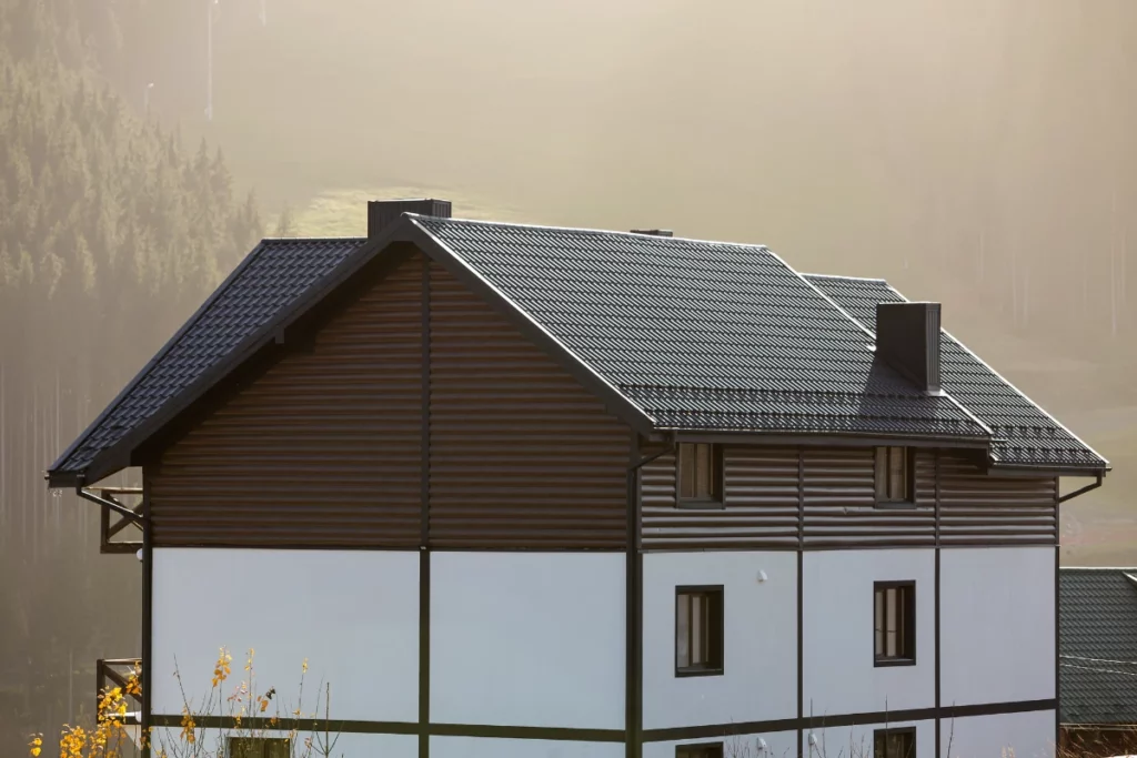 nice white and brown two-storied cottage with shingle roof in ecological area on foggy wood and hills background on sunny summer day. well maintained property, real estate concept.