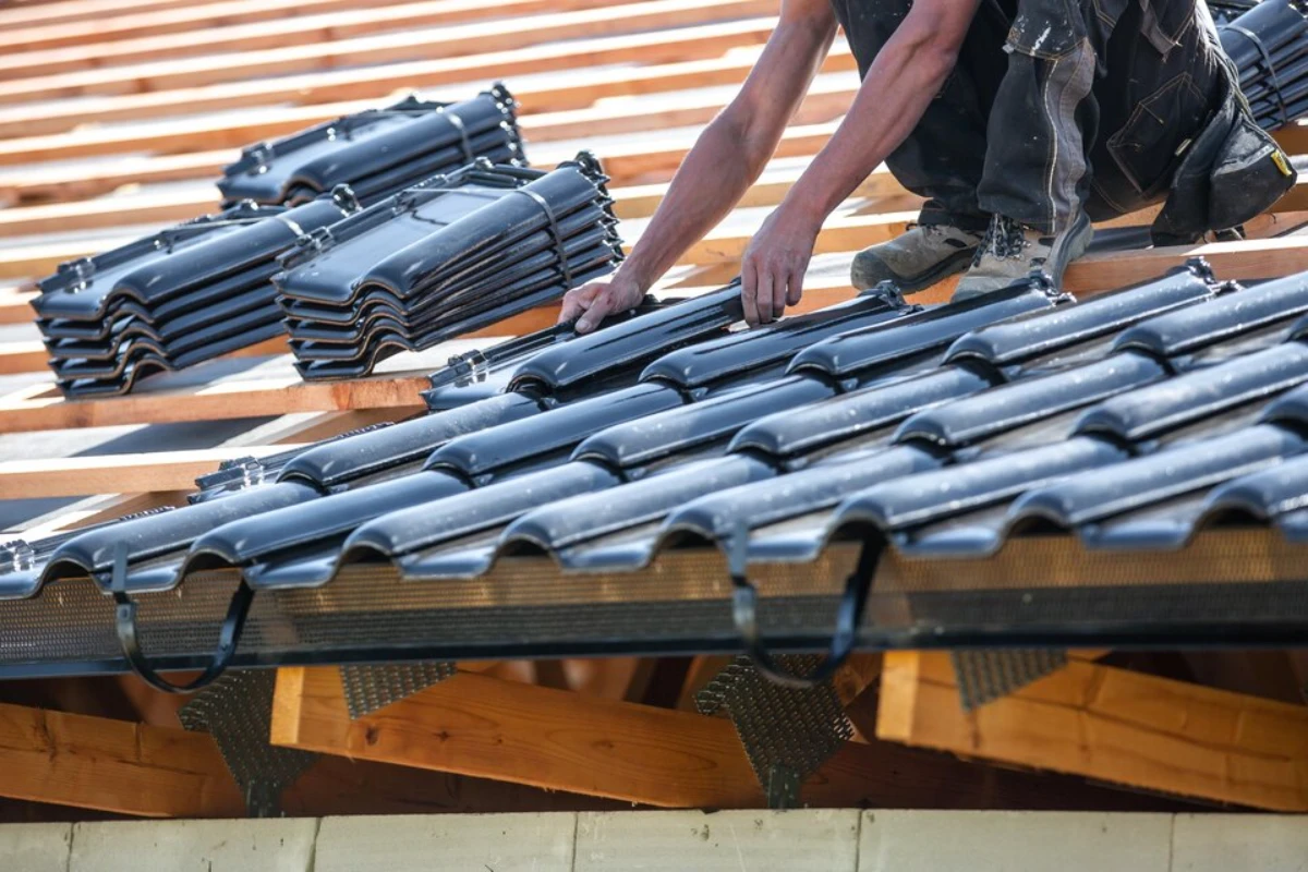 A man installs metal roofing on a sloped roof, wearing safety gear and focused on his work.